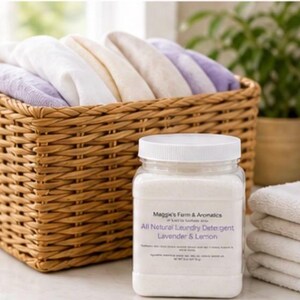 Puede incluir: Un frasco de pl&aacute;stico transparente con detergente para ropa y tapa blanca est&aacute; junto a una pila de toallas blancas. El frasco tiene una etiqueta que dice "All Natural Laundry Detergent Lavender & Lemon". Una cesta tejida llena de toallas dobladas est&aacute; en el fondo.