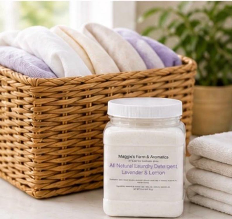 Puede incluir: Un frasco de pl&aacute;stico transparente con detergente para ropa y tapa blanca est&aacute; junto a una pila de toallas blancas. El frasco tiene una etiqueta que dice "All Natural Laundry Detergent Lavender & Lemon". Una cesta tejida llena de toallas dobladas est&aacute; en el fondo.