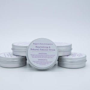 May include: A collection of small, silver-colored tins of cuticle cream. The central tin displays the text "Maggie's Farm & Aromatics Nourishing & Natural Cuticle Cream". The other tins are stacked around the central tin.