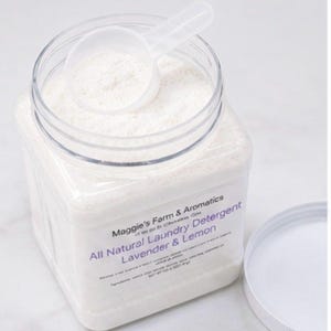 Puede incluir: Un recipiente cuadrado transparente de detergente blanco para ropa con una cuchara a juego encima. La etiqueta dice "All Natural Laundry Detergent Lavender & Lemon". La tapa est&aacute; a un lado.