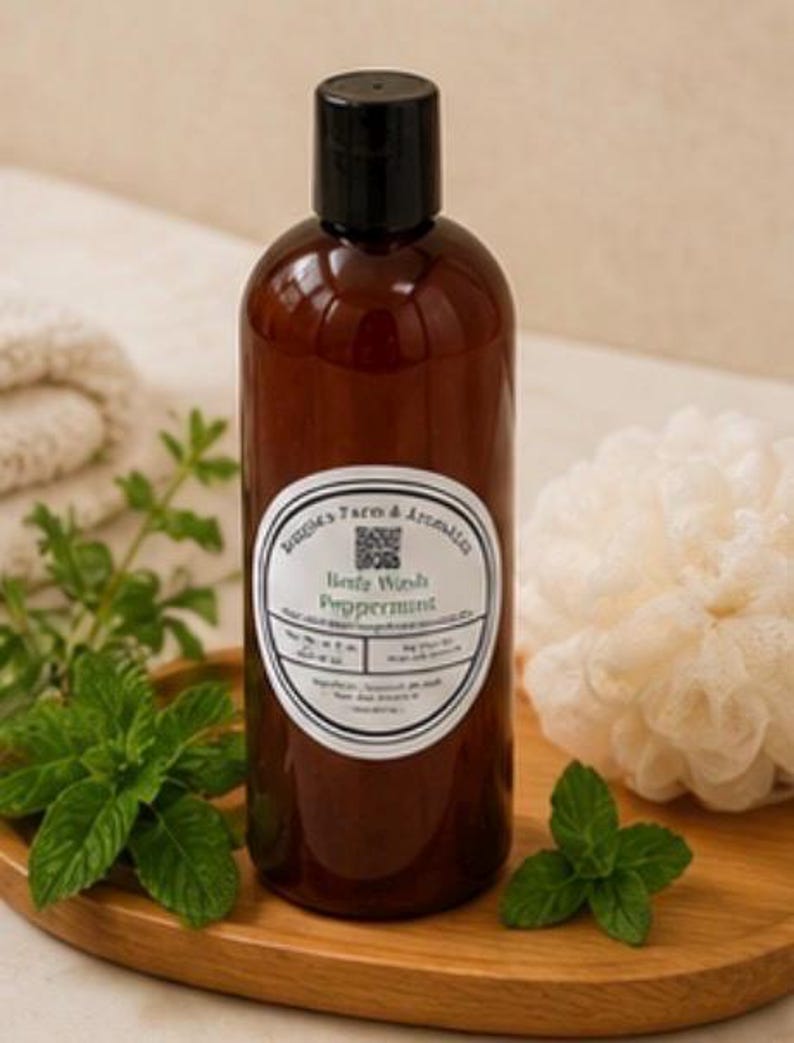 May include: A brown bottle of body wash with a black cap and a white label that reads "Body Wash Peppermint." Fresh mint leaves and a loofah are on a wooden tray. The bottle is surrounded by fresh mint leaves and a white loofah.