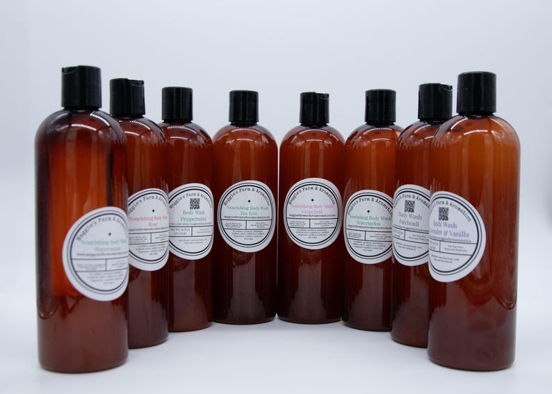May include: A collection of brown plastic bottles with black caps, each labeled with a white and blue circular sticker. The labels read "Nourishing Body Wash" with various scents like Rose, Peppermint, and Lavender & Vanilla. The bottles are arranged against a white background.