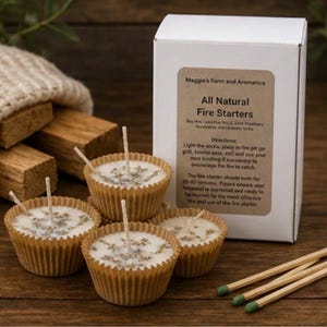 May include: A collection of natural fire starters in cupcake-shaped molds, with a white box labeled "Maggie's Farm and Aromatics." The fire starters are accompanied by wooden matches and wood pieces. The text on the box reads "All Natural Fire Starters."