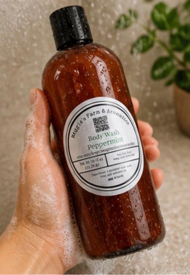 May include: A brown body wash bottle with a black cap is held in a soapy hand. The label reads "Peppermint Body Wash" from "Haugle's Farm & Aromatics". The bottle is wet with water droplets, suggesting use in a shower.