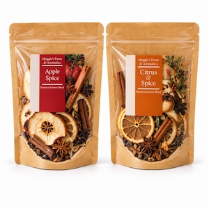 May include: Two stand-up pouches with clear windows containing botanical simmer blends. The left pouch is labeled Maggie's Farm & Aromatics Apple Spice, featuring dried apple slices, cinnamon sticks, and star anise. The right pouch is labeled Maggie's Farm & Aromatics Citrus & Spice, containing dried orange slices, cinnamon sticks, and star anise.