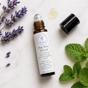 May include: A brown glass roll-on bottle labeled "Bug Bite Relief" with a black cap, next to a lavender sprig and mint leaves. The label lists ingredients and the bottle contains 10ml or .34 fl oz of product.