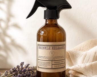 May include: An amber glass spray bottle with a black trigger nozzle. The label reads WRINKLE RELEASER, Lavender Scent, and 8 FL OZ (236.6 ml). The bottle contains a liquid solution and is labeled with ingredients including distilled water and glycerin.