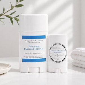 Puede incluir: Dos barras de desodorante blancas, una grande y otra pequeña, se muestran sobre una superficie blanca. La barra más grande tiene una etiqueta azul con el texto "Unscented Natural Deodorant". La barra más pequeña tiene una etiqueta circular que dice "Homemade Deodorant Unscented".