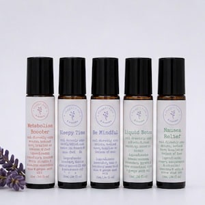 May include: Five essential oil roller bottles with black caps and white labels. The labels feature text such as "Metabolise Booster", "Sleepy Time", and "Nausea Relief". A sprig of lavender is visible on the left.