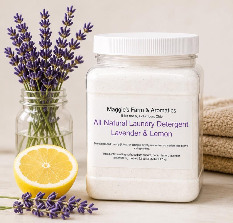 Puede incluir: Un frasco transparente de detergente para ropa natural con tapa blanca, etiquetado como "Lavanda y Lim&oacute;n". Una ramita de lavanda y media rodaja de lim&oacute;n est&aacute;n junto al frasco. La etiqueta incluye el texto "Maggie's Farm & Aromatics".