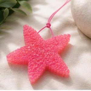 May include: A bright pink, five-pointed starfish-shaped air freshener. The surface has a textured, bubbly appearance. A pink string is attached for hanging. The background is a soft, neutral fabric.