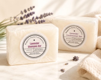 Op de afbeelding: Twee rechthoekige, gebroken witte zeepblokken, de ene met het label Lavender Shampoo Bar en de andere Lavender Conditioner Bar van Maggie's Farm & Aromatics. Elk blok weegt 127 g en is verpakt in doorzichtig plastic.
