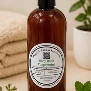 May include: A brown bottle of peppermint body wash with a black cap. The label reads "Maggie's Farm & Aromatics Body Wash Peppermint." A stack of folded beige towels and a potted plant are in the background.