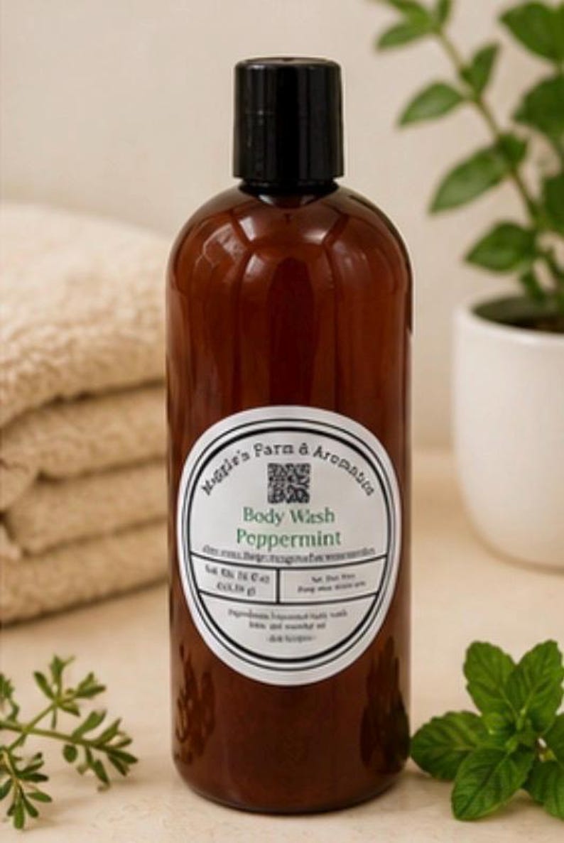 May include: A brown bottle of peppermint body wash with a black cap. The label reads "Maggie's Farm & Aromatics Body Wash Peppermint." A stack of folded beige towels and a potted plant are in the background.