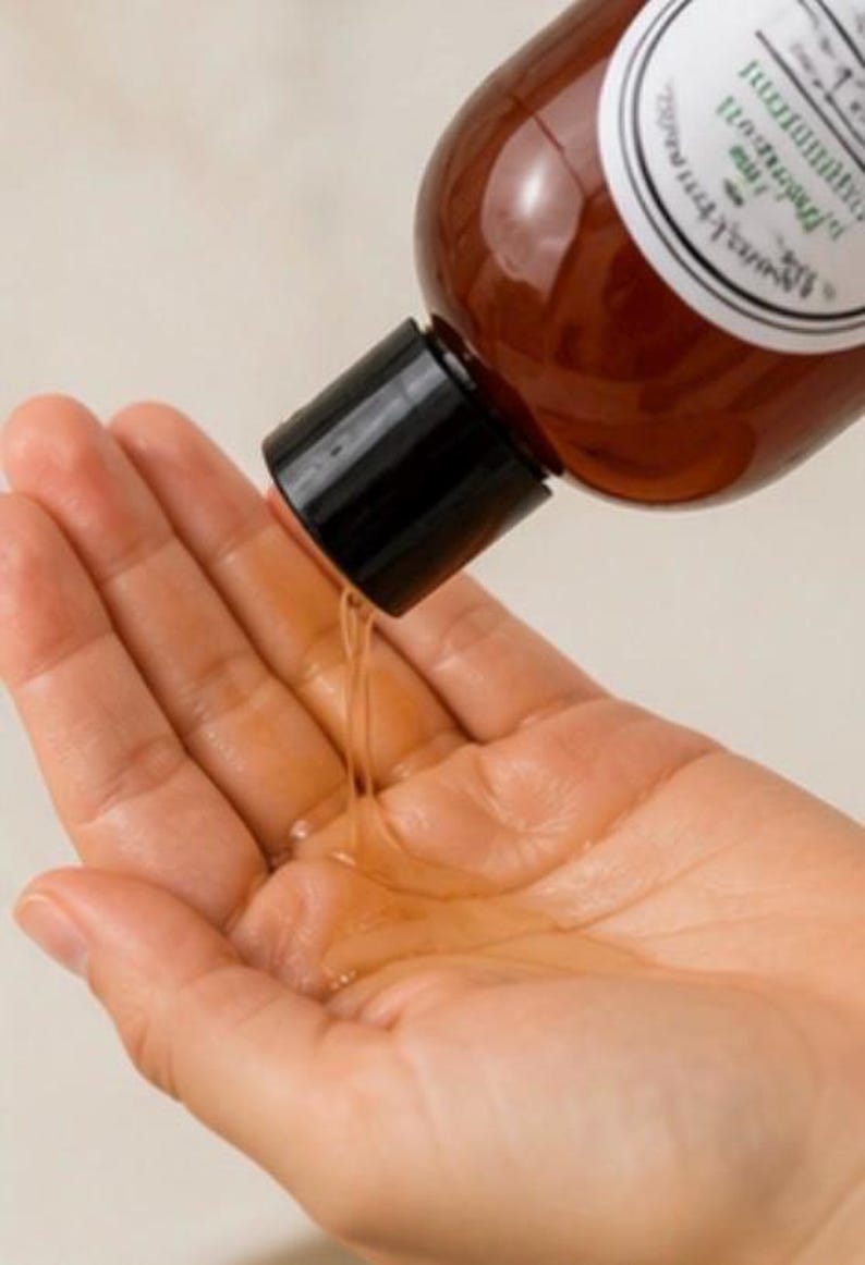 May include: A brown bottle with a black cap is pouring a clear liquid into a hand. The bottle has a white label with black text. The liquid is a light amber color.