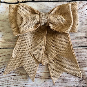 May include: A large, brown burlap bow with two long tails. The bow is tied in a knot and the tails are frayed at the ends.