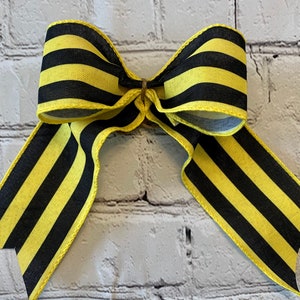 May include: A black and yellow striped bow with a simple, classic design. The bow is made from a thick, textured fabric and is tied with a single knot in the centre.