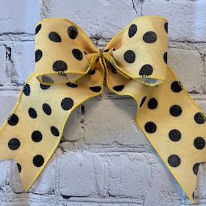 May include: A yellow bow with black polka dots. The bow is made of a soft, silky fabric and has a wired edge.