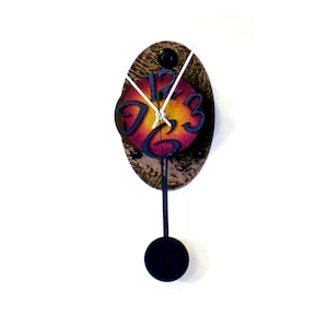 May include: A pendulum clock with a round, oval-shaped face. The face is painted with a gradient of orange, red, and yellow. The numbers are black and stylized. The clock has a black pendulum and a black metal frame.