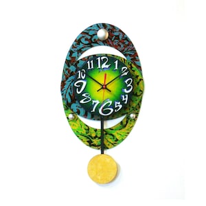 May include: A green and blue oval-shaped wall clock with a pendulum. The clock face has a green background with black numbers and a red hour hand and black minute hand.