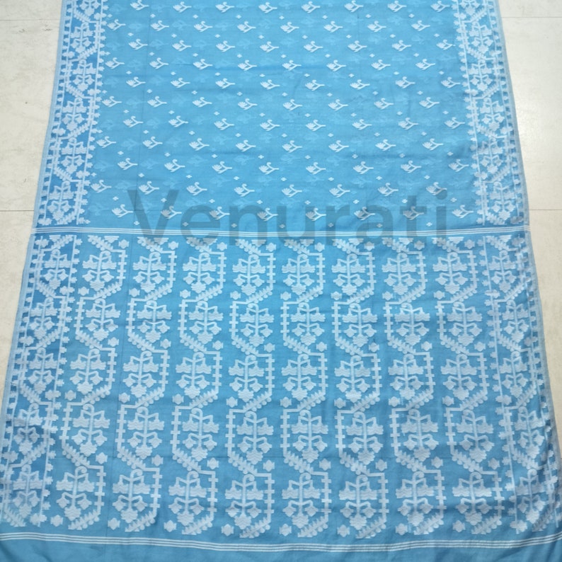 May include: A light blue saree with a white floral pattern. The saree has a border with a repeating geometric design.