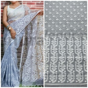 May include: A gray and white saree with a floral pattern. The saree is made of a sheer fabric and has a delicate, intricate design.