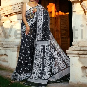 May include: A black and white saree with a geometric pattern. The saree is made of a sheer fabric and has a silver border.