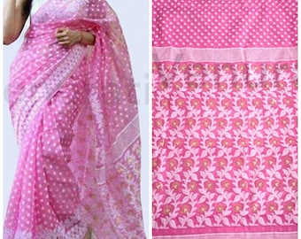 May include: A pink and white cotton saree with a floral pattern. The saree has a white border with small pink dots. The saree is draped on a woman.