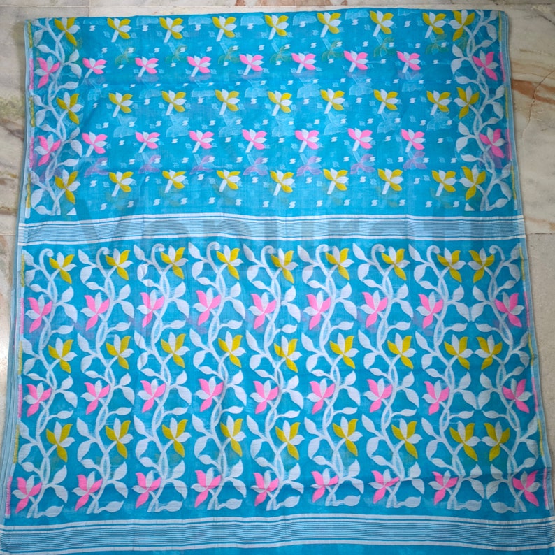 May include: A blue saree with a white and pink floral pattern. The saree has a traditional Indian design and is made of a lightweight fabric.