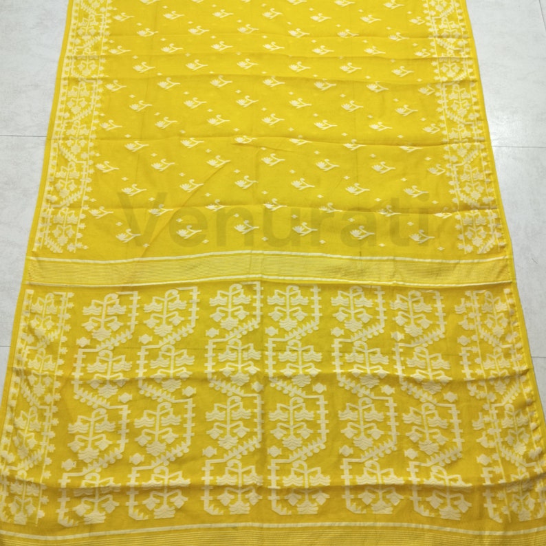 May include: A yellow cotton saree with a white floral pattern. The saree has a border with a white floral design.