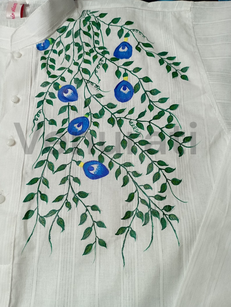 May include: A white shirt with a hand-painted design of blue flowers and green vines. The design is on the front of the shirt, near the collar.