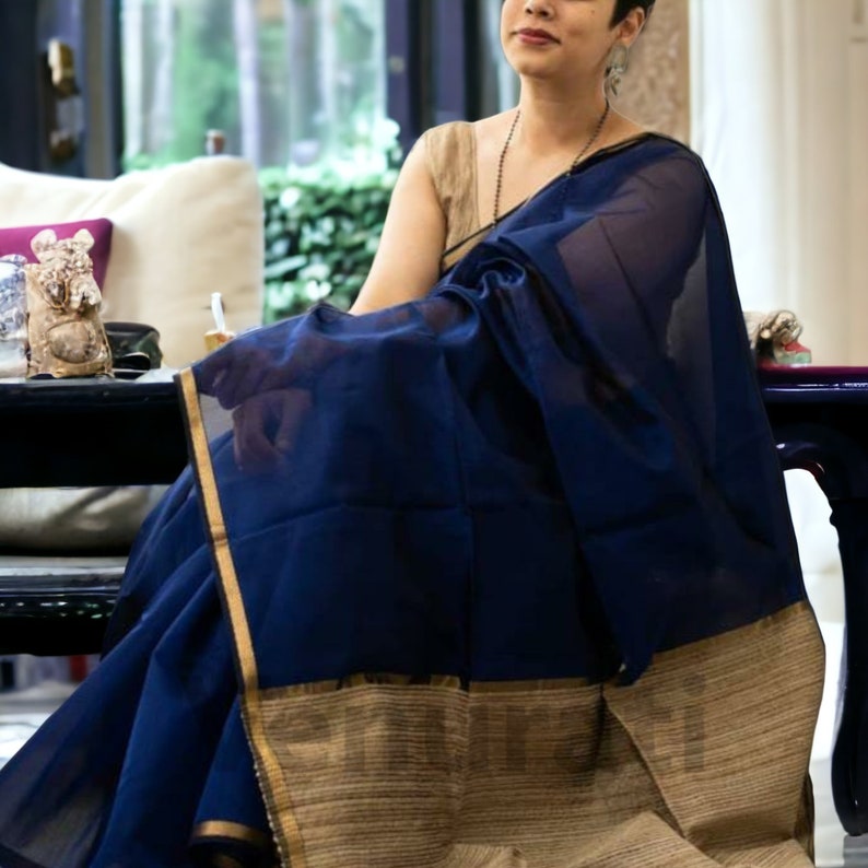 May include: A navy blue saree with a gold border and a beige and gold striped pallu. The saree is draped over a person's body.