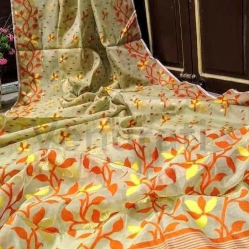May include: A light green sheer saree with a floral pattern in orange and yellow. The saree has a delicate, flowing texture.