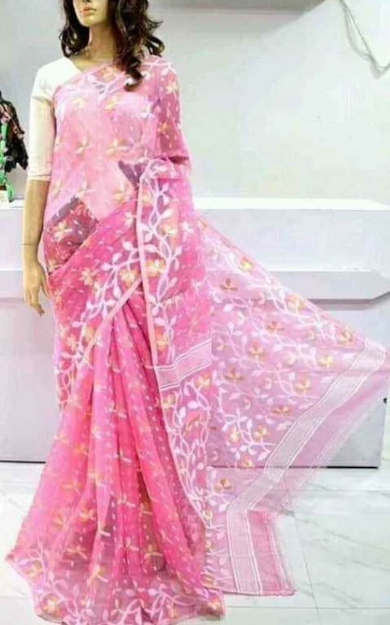 May include: A pink sheer saree with white floral embroidery. The saree is draped on a person and has a white border.