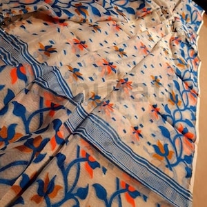 May include: A white saree with a blue, orange, and brown floral pattern. The saree has a blue and white striped border.