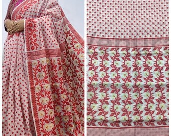 May include: White and red cotton saree with a polka dot pattern and floral design. The saree has a red border with a white and red floral pattern.