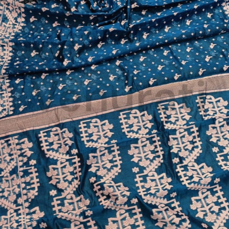 May include: A teal blue silk saree with a white floral pattern. The saree has a border with a silver and white design.