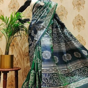 May include: A green and blue silk saree with a white block print design. The saree is draped on a mannequin and features intricate floral and geometric patterns.