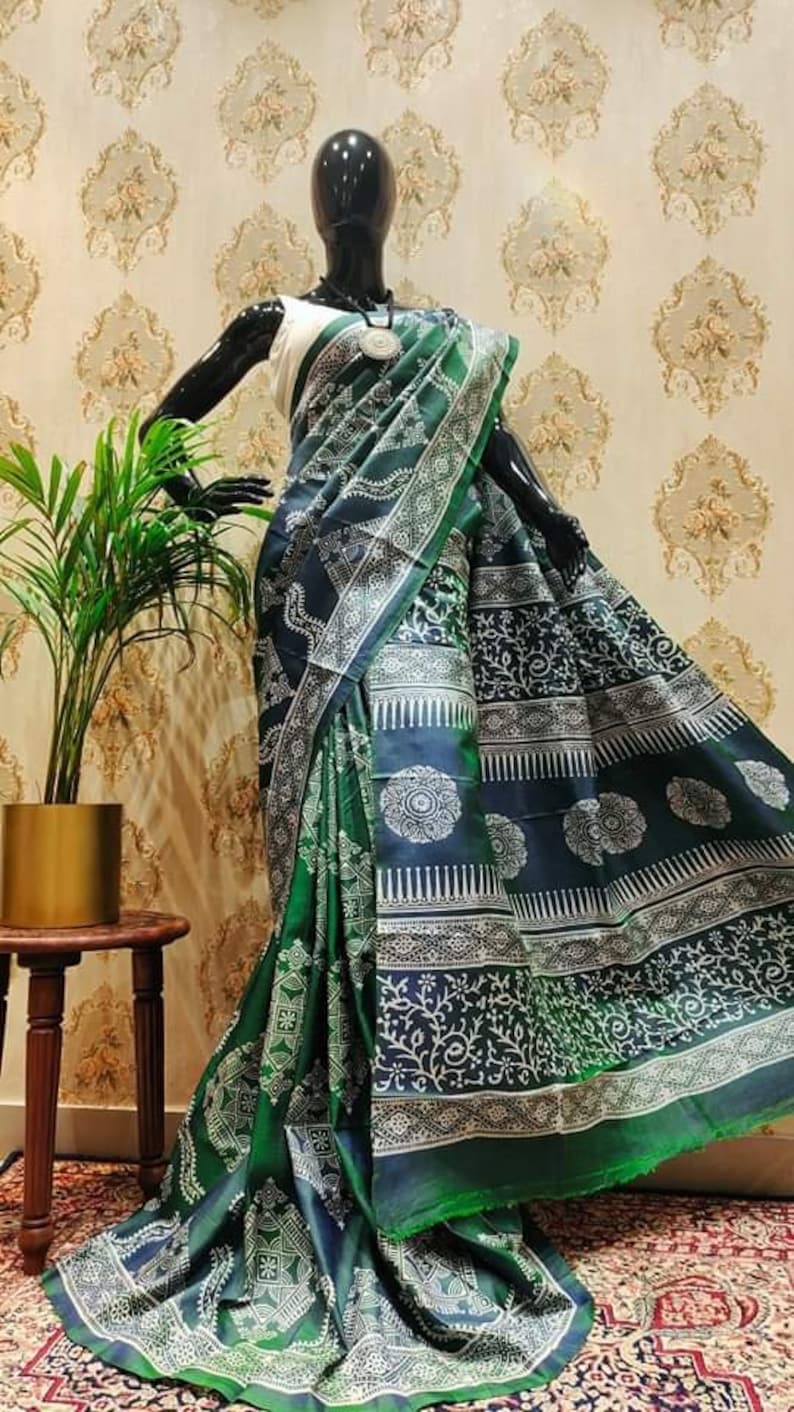 May include: A green and blue silk saree with a white block print design. The saree is draped on a mannequin and features intricate floral and geometric patterns.
