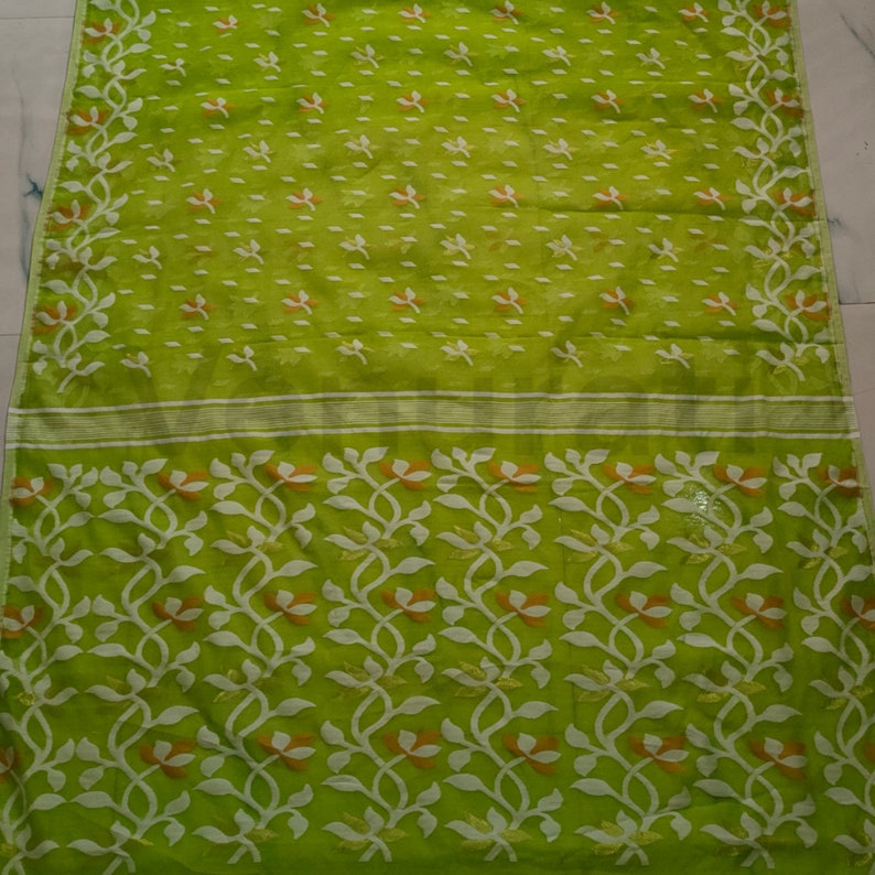 May include: A green and white saree with a floral pattern. The saree has a light green base with white and orange floral designs.