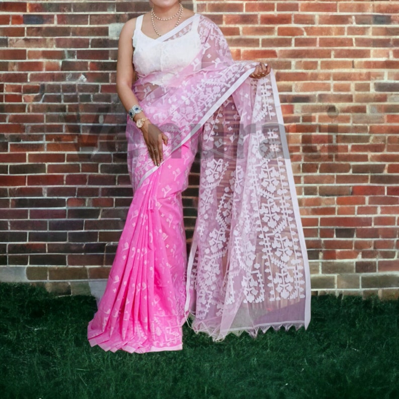 May include: A pink and white saree with intricate white embroidery. The saree is draped over a person's body and is worn with a white sleeveless blouse.