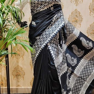 May include: A black and white patterned saree with a geometric design. The saree is draped on a mannequin and has a white border with a paisley pattern.