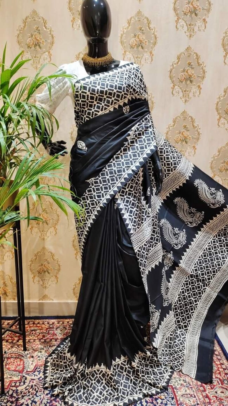 May include: A black and white patterned saree with a geometric design. The saree is draped on a mannequin and has a white border with a paisley pattern.