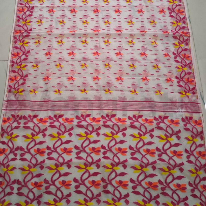 May include: White saree with a pink and orange floral pattern. The saree has a white border with a pink and orange floral design.