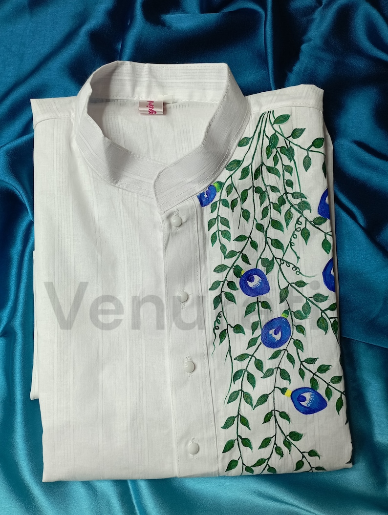 May include: White long-sleeved shirt with a mandarin collar and a hand-painted design of blue flowers and green leaves on the right side. The shirt has a label that says "girl".