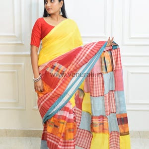 May include: A woman wearing a yellow saree with a red, blue, and white checkered pattern. The saree has a patchwork design with different colored squares. The woman is wearing a red blouse.