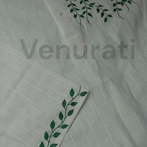 May include: White shirt with green leaf designs painted on the collar and cuff. The shirt has a striped pattern.