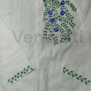 May include: White long-sleeved shirt with green vines and blue flowers painted on the front. The shirt has a mandarin collar and button closure. The sleeves have green vines painted on the cuffs.
