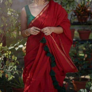 May include: A woman wearing a red sari with a green blouse and green tassels. The sari has a gold border and a gold stripe running down the centre.