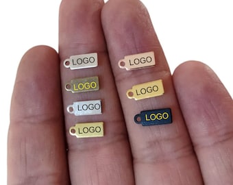 Può includere: Sei piccoli cartellini metallici con la parola "LOGO" stampata in giallo su ogni cartellino. I cartellini sono di diversi colori: argento, oro, ottone, nero e due tonalità di grigio.